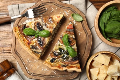 Pieces of delicious quiche with mushrooms and ingredients on wooden table, flat lay