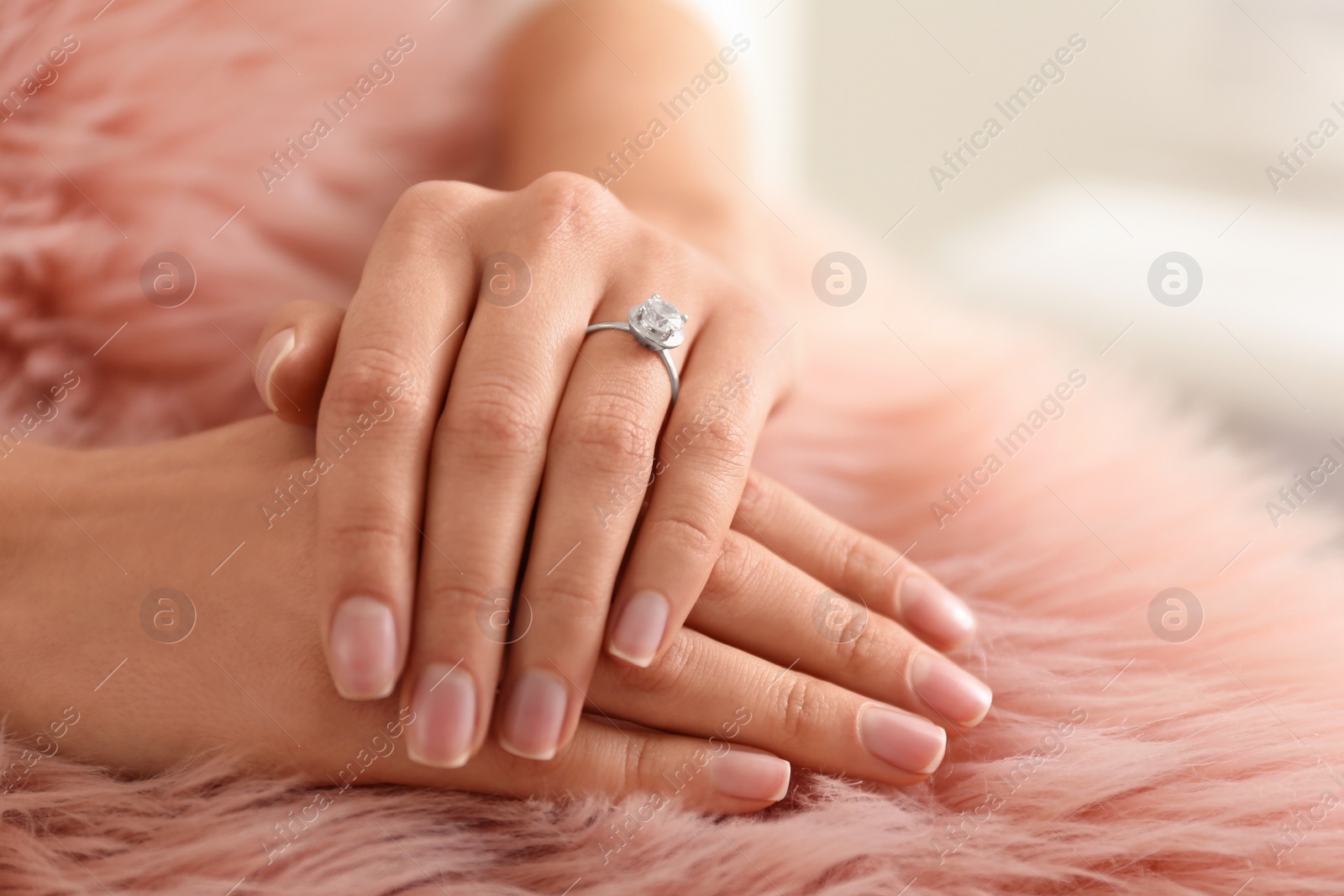 Photo of Young woman wearing beautiful engagement ring on faux fur rug, closeup