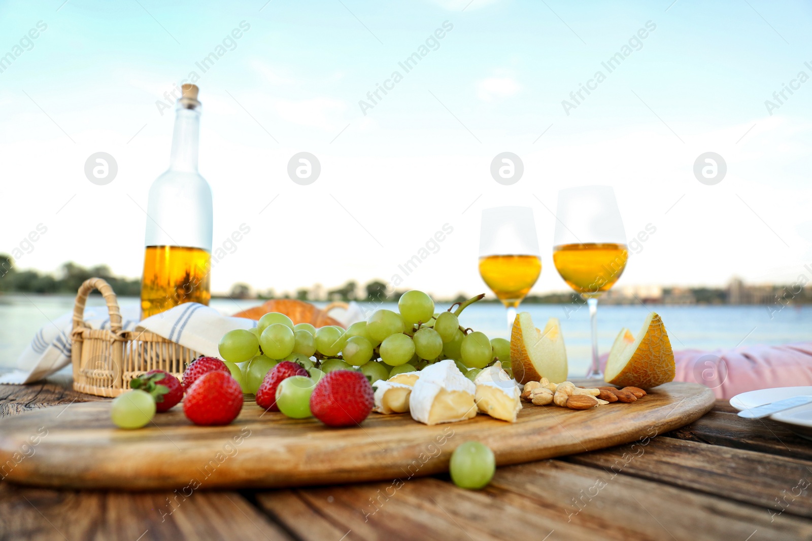 Photo of Food for picnic and white wine served on wooden pallet near river