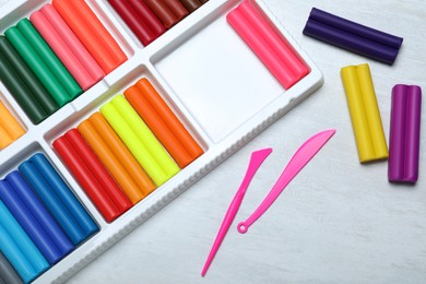 Photo of Colorful plasticine and tools on white table, flat lay