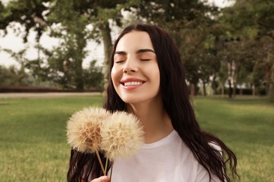 Beautiful young woman with large dandelions in park. Allergy free concept