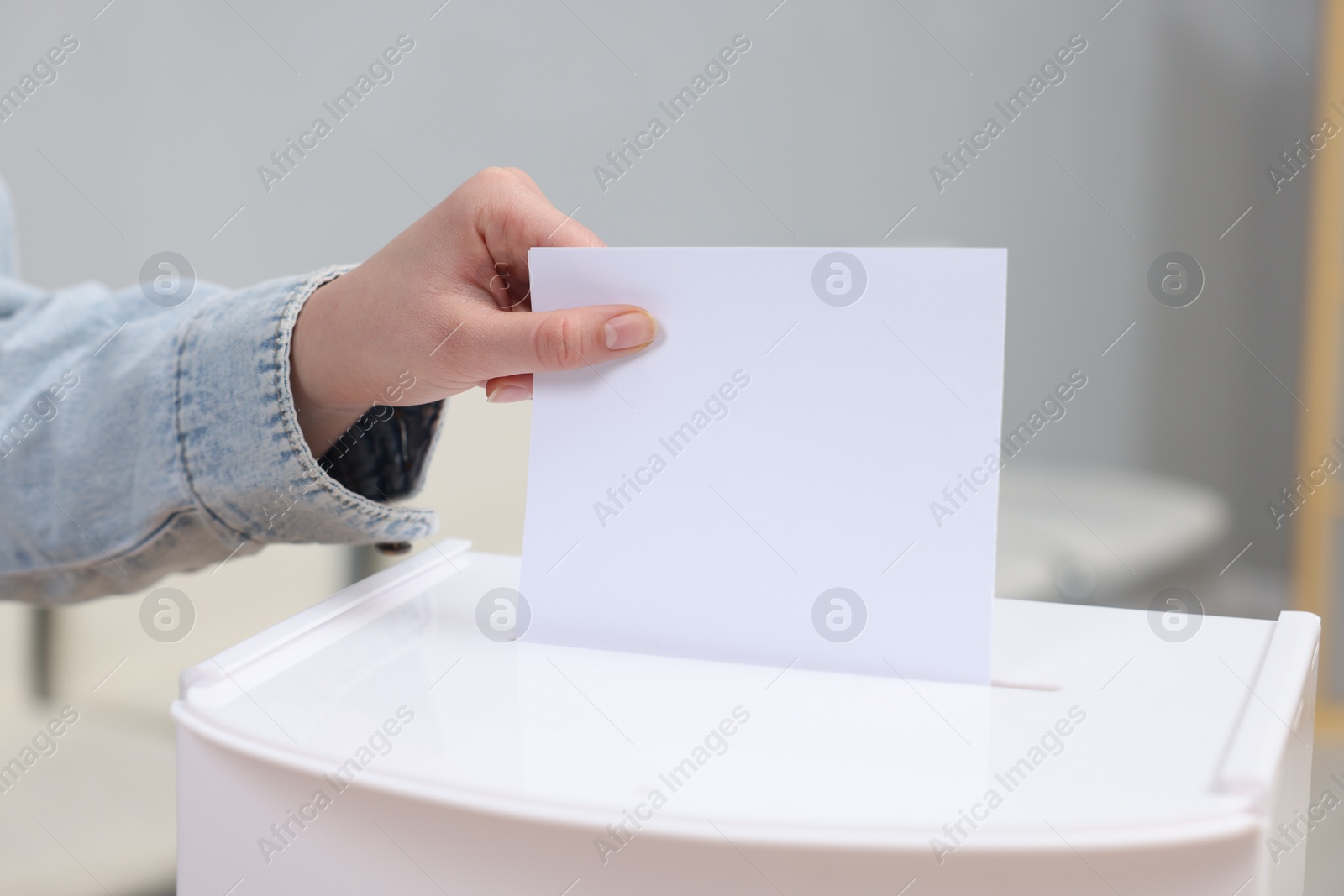 Photo of Woman putting her vote into ballot box on blurred background, closeup