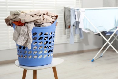 Photo of Plastic laundry basket overfilled with clothes on white stool indoors. Space for text