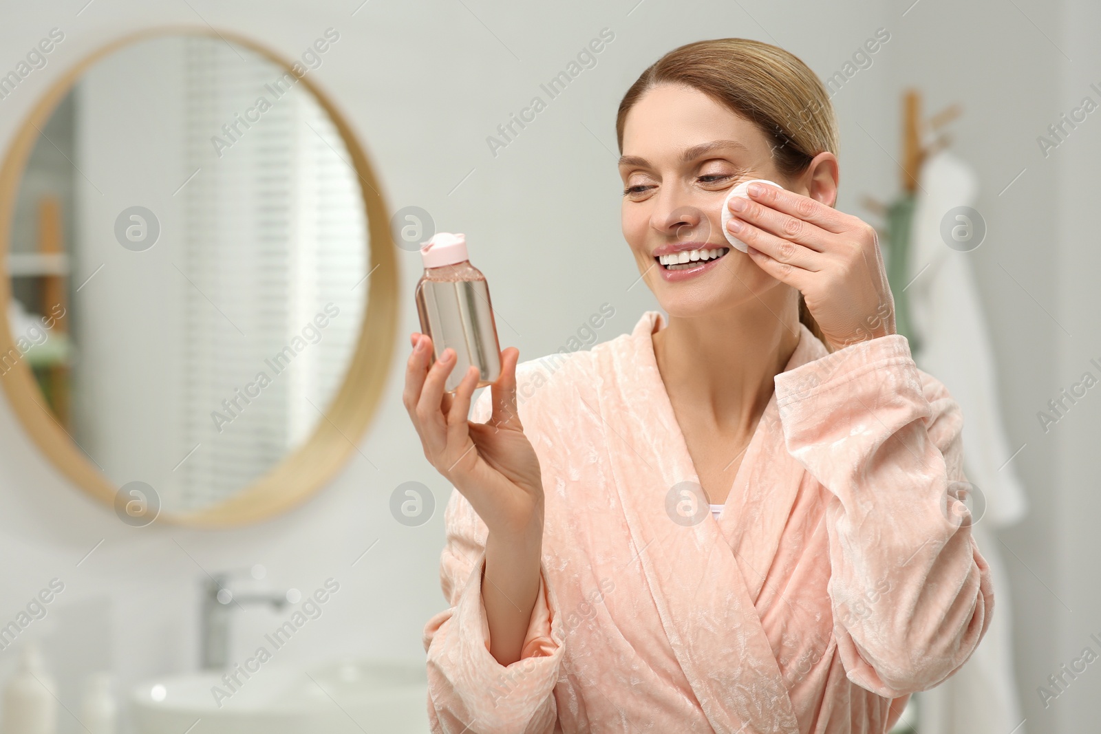 Photo of Beautiful woman removing makeup with cotton pad indoors, space for text