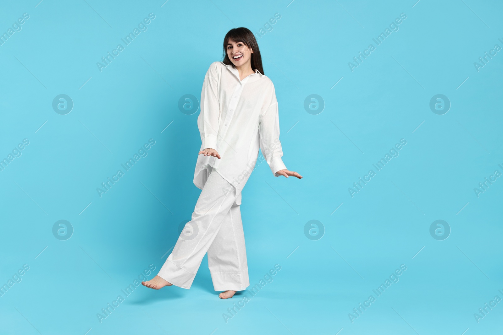 Photo of Happy woman wearing pyjama on light blue background