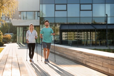 Photo of Happy couple practicing Nordic walking with poles outdoors