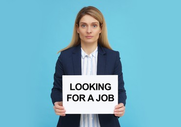 Unemployed woman holding sign with phrase Looking For A Job on light blue background