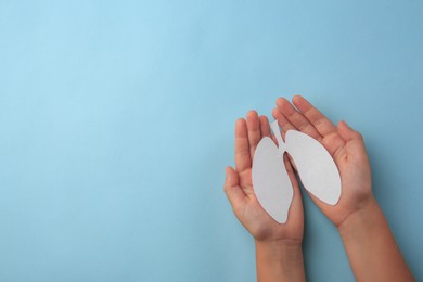 Photo of Child holding paper human lungs on light blue background, top view. Space for text