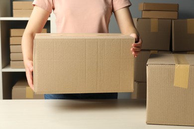 Photo of Packaging goods. Woman with cardboard boxes at white table indoors, closeup