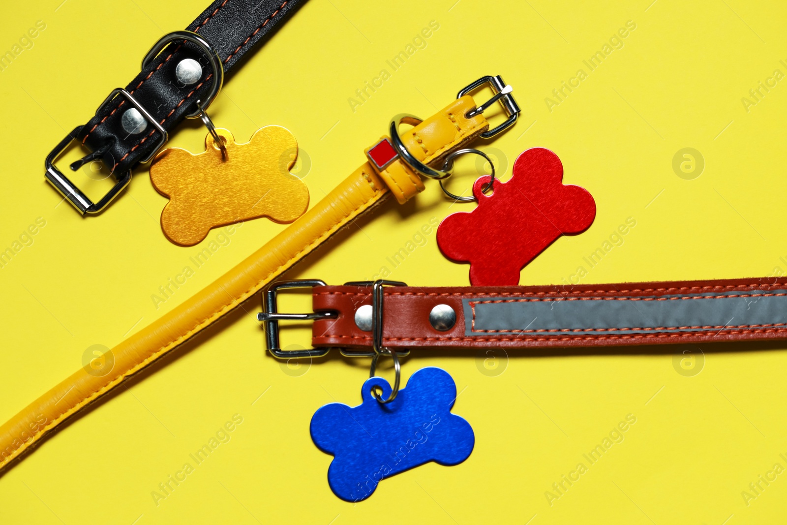 Photo of Color leather dog collars with tags in shape of bone on yellow background, flat lay