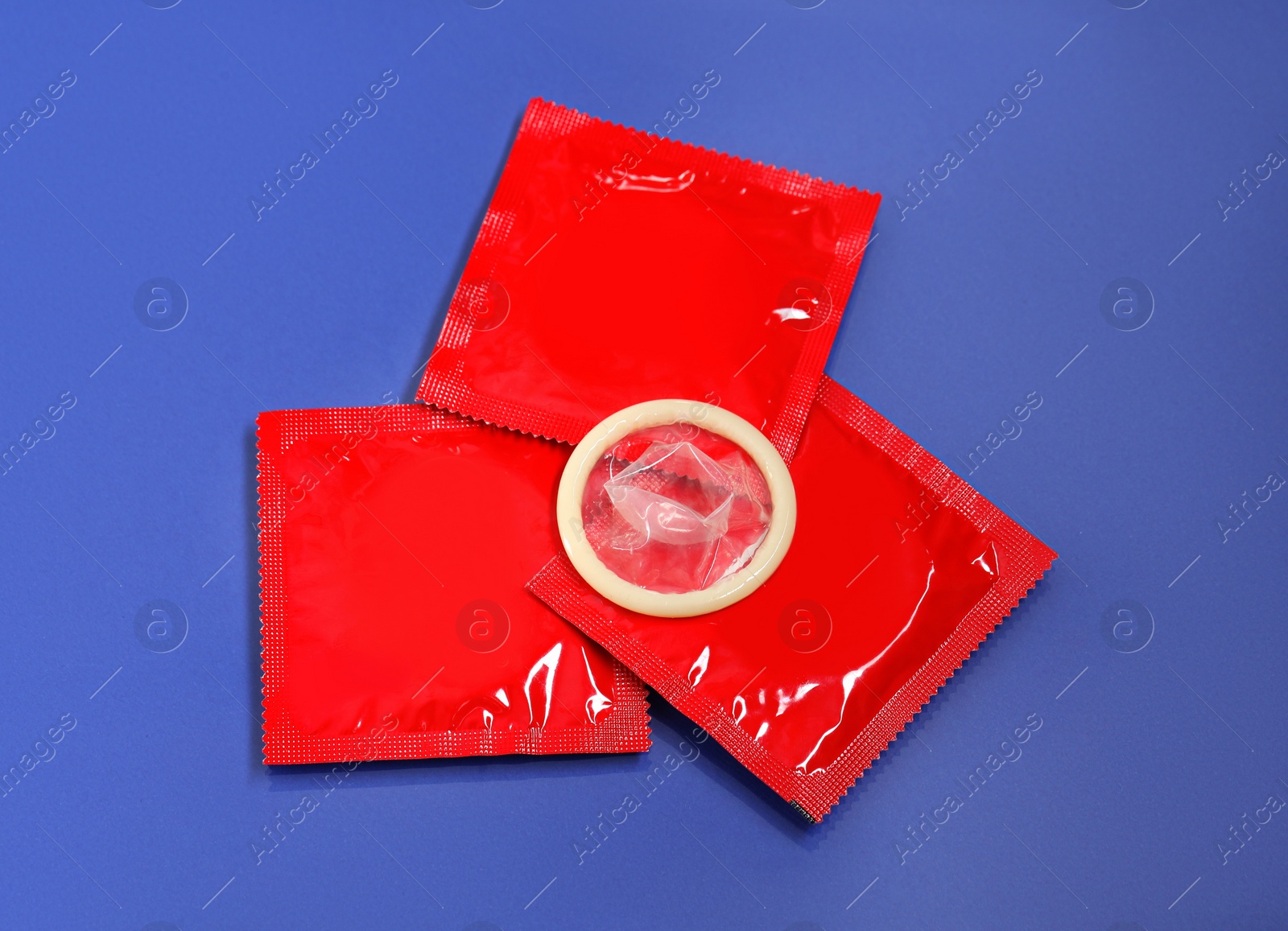 Photo of Unpacked condom and packages on blue background, flat lay. Safe sex