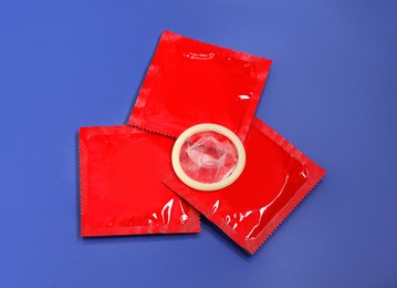 Unpacked condom and packages on blue background, flat lay. Safe sex