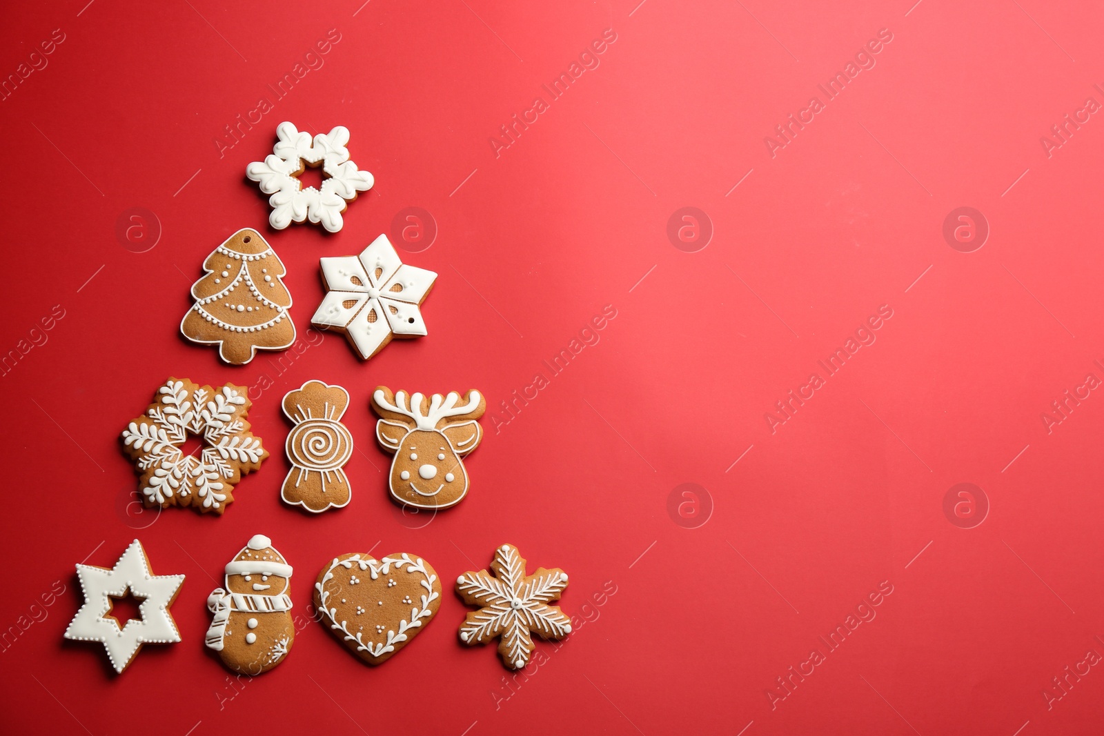 Photo of Delicious gingerbread cookies arranged in shape of Christmas tree on red background, flat lay. Space for text