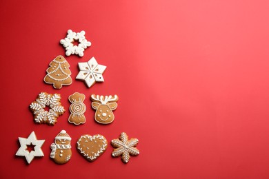 Photo of Delicious gingerbread cookies arranged in shape of Christmas tree on red background, flat lay. Space for text