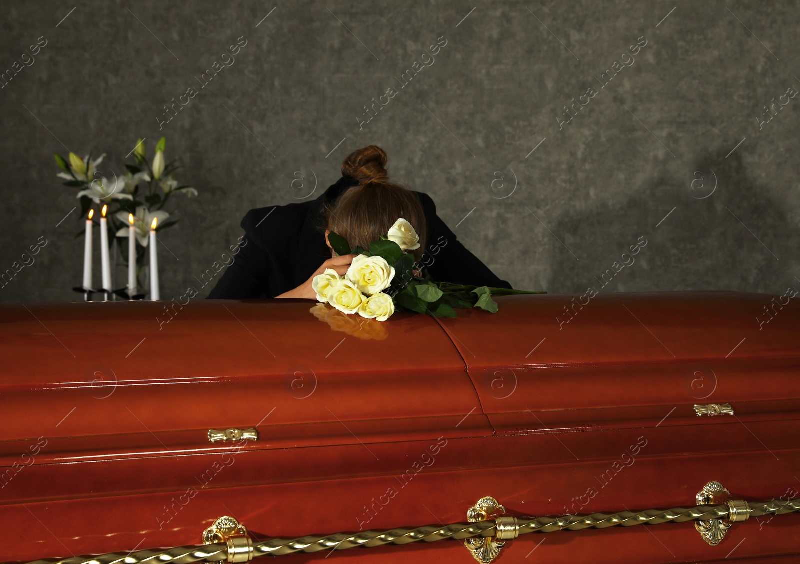 Photo of Sad woman mourning near casket with white roses in funeral home