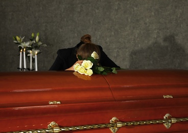 Photo of Sad woman mourning near casket with white roses in funeral home