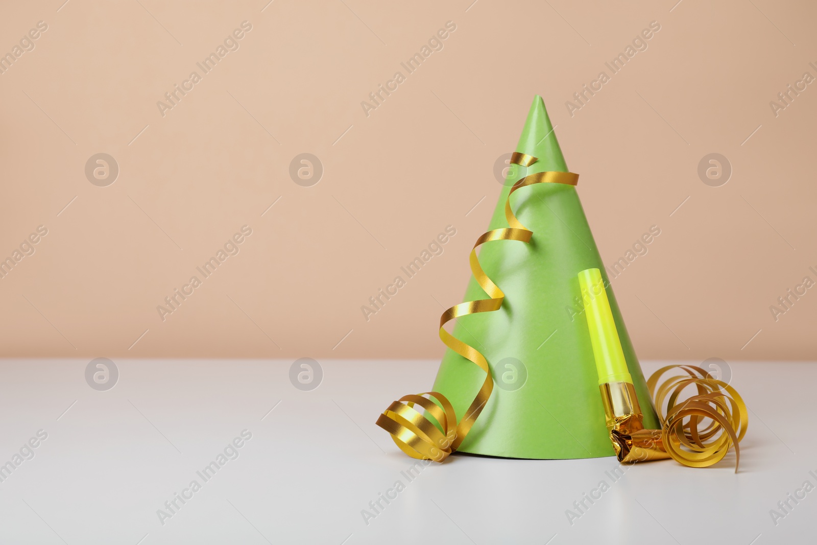 Photo of Colorful party hat, streamers and blower on white table, space for text. Birthday celebration