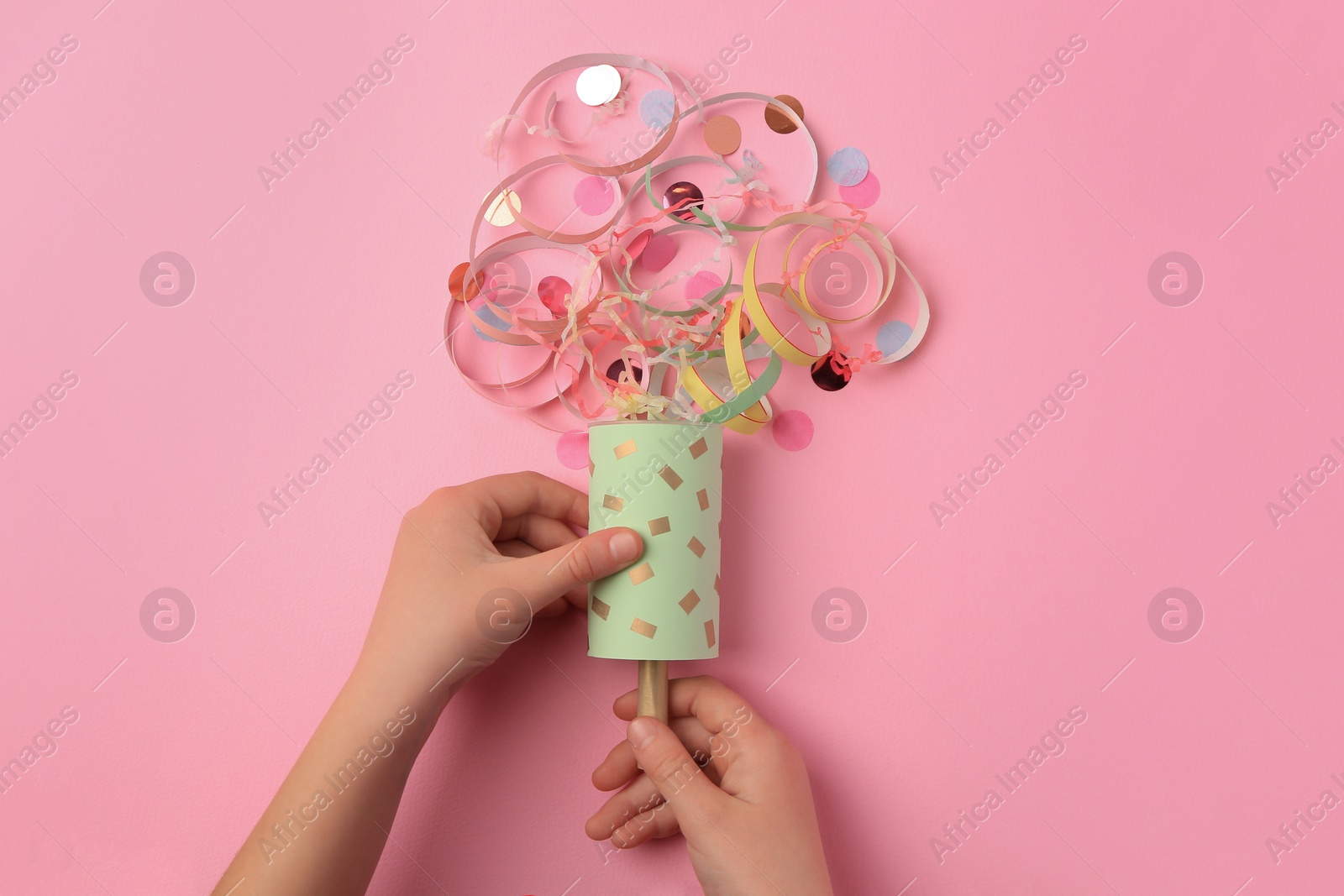 Photo of Woman holding party popper with serpentine and confetti on pink background, top view