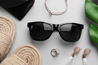 New stylish sunglasses with black leather case, wicker slippers and beautiful jewelry on white table, flat lay