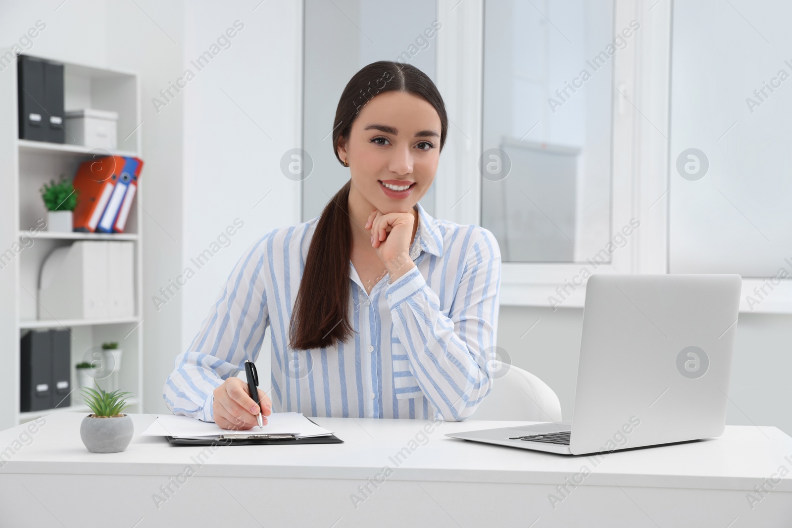 Photo of Young female intern working with laptop at table in office