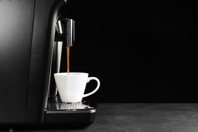 Photo of Modern espresso machine pouring coffee into cup on grey table against black background. Space for text