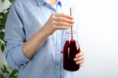 Photo of Woman with bottle of fresh beet juice on light background, closeup