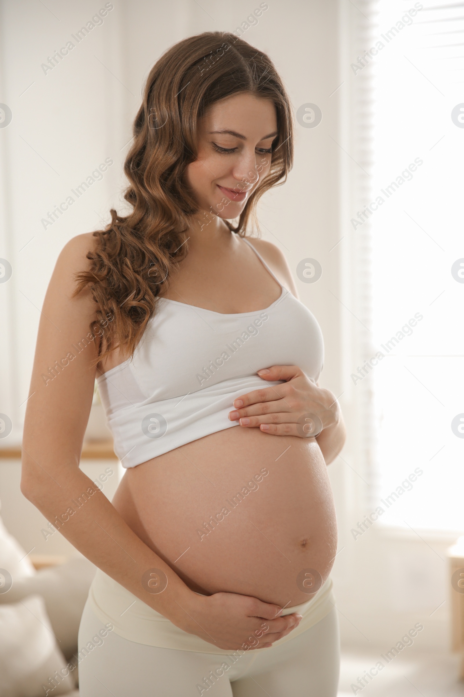 Photo of Happy pregnant woman touching her belly indoors