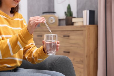 Photo of Woman dripping food supplement into glass of water indoors, closeup. Space for text