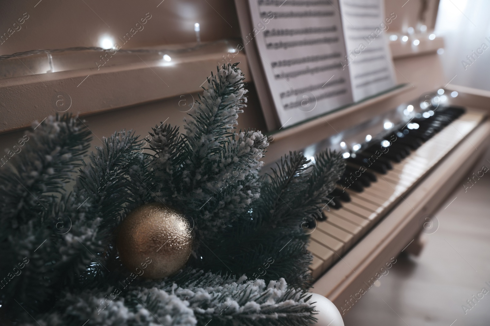 Photo of Fir branches with bauble on white piano indoors, closeup. Christmas music
