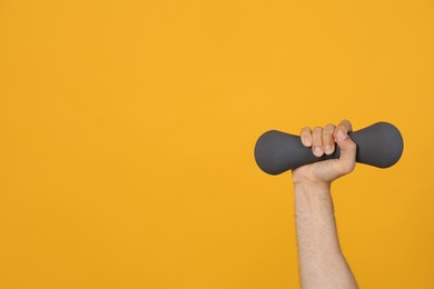 Photo of Man holding dumbbell on orange background, closeup. Space for text