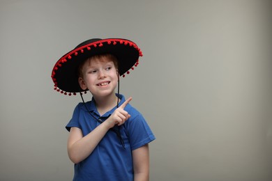 Photo of Cute boy in Mexican sombrero hat pointing at something on grey background, space for text