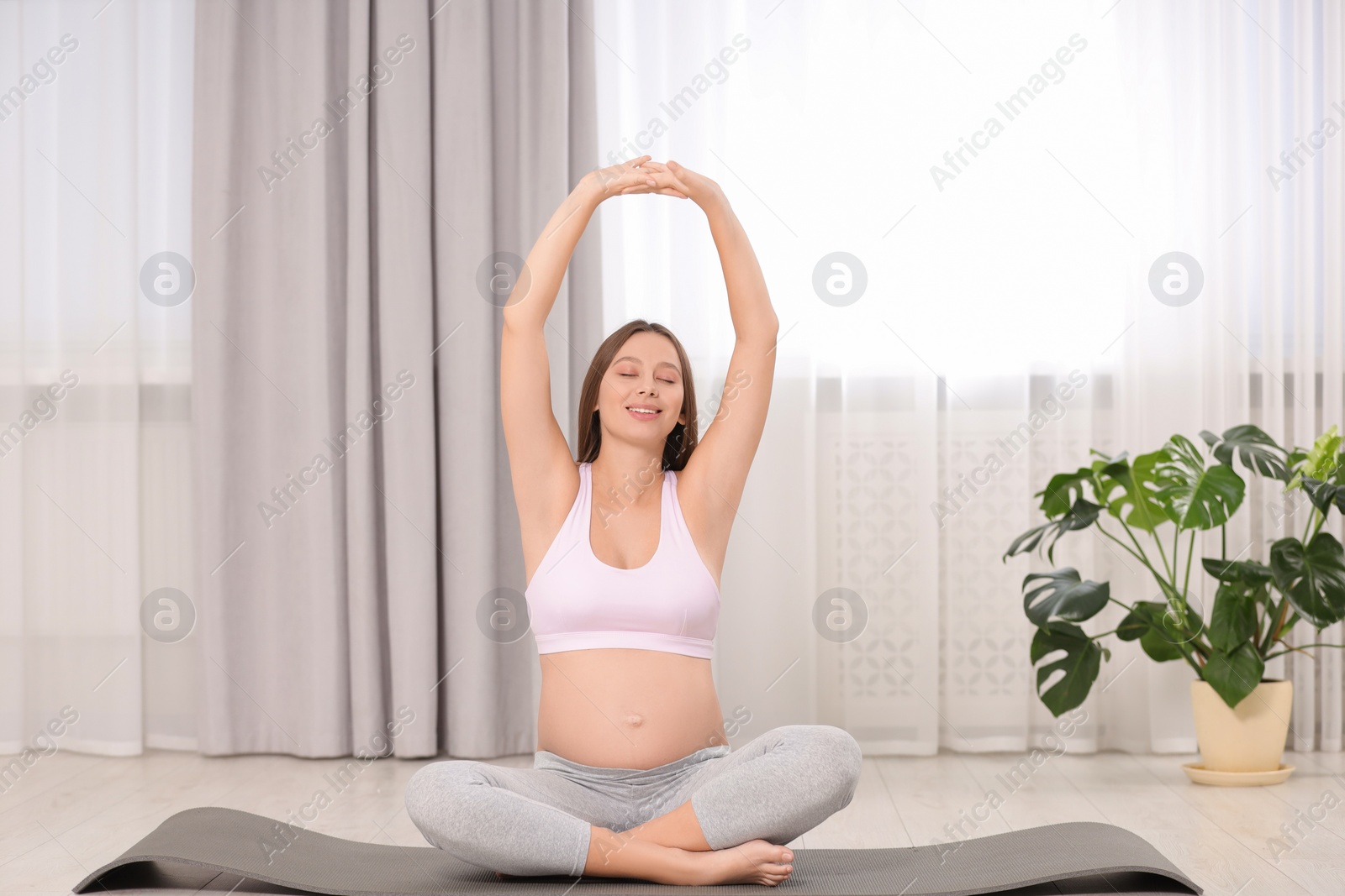 Photo of Pregnant woman doing exercises on yoga mat at home