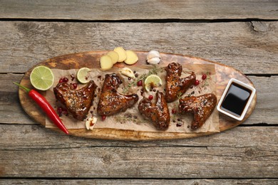 Photo of Tasty chicken wings glazed in soy sauce with garnish on wooden table, top view