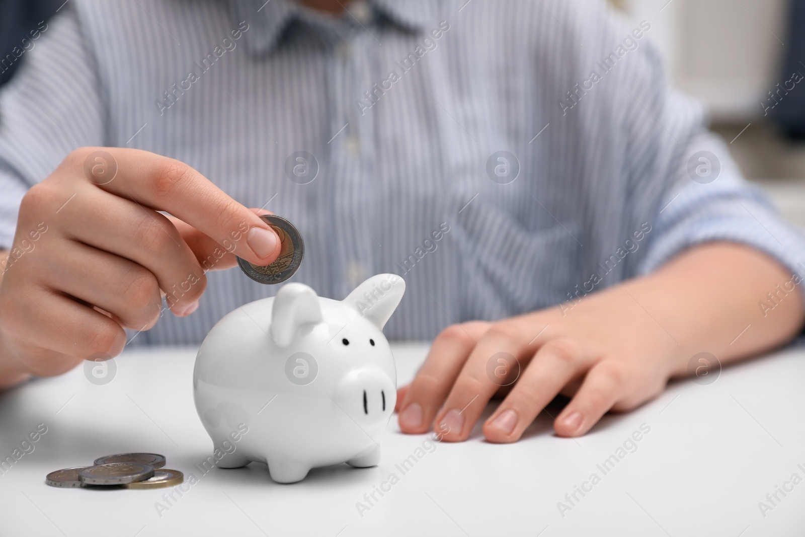 Photo of Woman putting coin into ceramic piggy bank at white wooden table, closeup. Financial savings