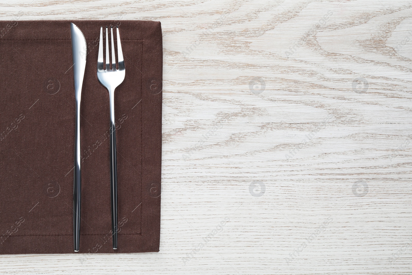 Photo of Fork, knife and napkin on white wooden table, top view with space for text. Stylish shiny cutlery set