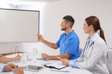 Photo of Team of doctors looking at projection screen indoors. 
Video conference