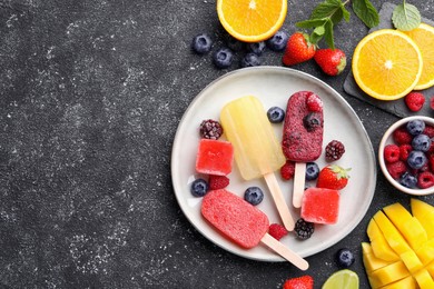 Photo of Plate of different fruit ice pops on black textured table, flat lay. Space for text