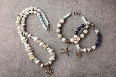 Different beautiful bracelets and necklace with gemstones on grey background, flat lay
