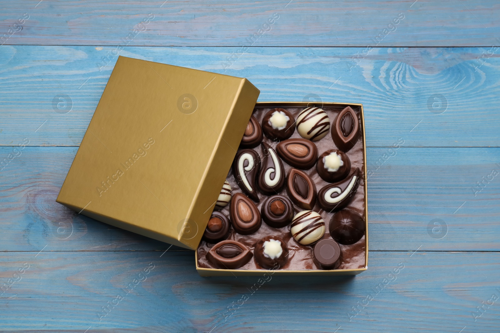 Photo of Open box of delicious chocolate candies on light blue wooden table, top view