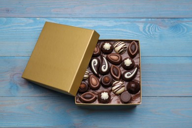 Open box of delicious chocolate candies on light blue wooden table, top view