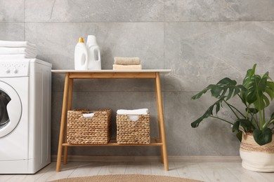 Photo of Storage baskets with towels, detergents, houseplant and washing machine indoors