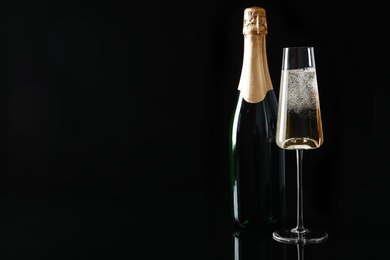 Bottle and glass of champagne on black background, space for text