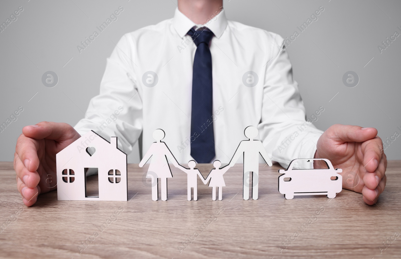 Photo of Man protecting figures of family, car and house at wooden table. closeup. Insurance concept