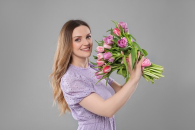 Photo of Happy young woman with bouquet of beautiful tulips on grey background