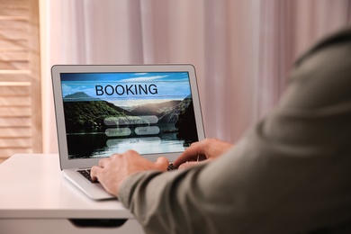 Photo of Man with laptop booking tickets online at white table, closeup. Travel agency concept