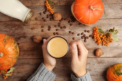 Photo of Woman holding cup of pumpkin spice latte on wooden background, top view