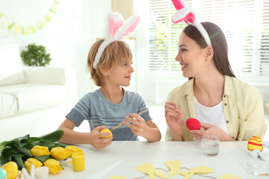 Happy mother and son with bunny ears headbands painting Easter eggs at home