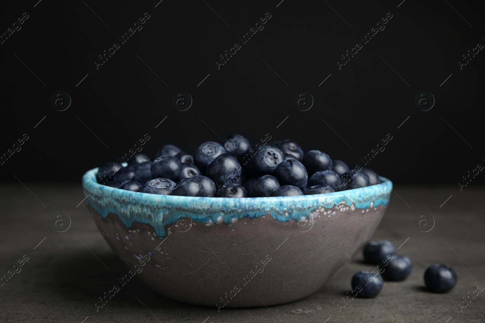 Photo of Bowl of tasty blueberries on grey table against black background