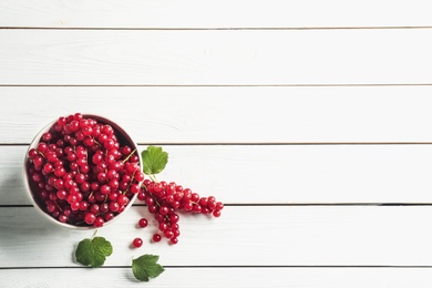 Photo of Delicious red currants and leaves on white wooden table, flat lay. Space for text