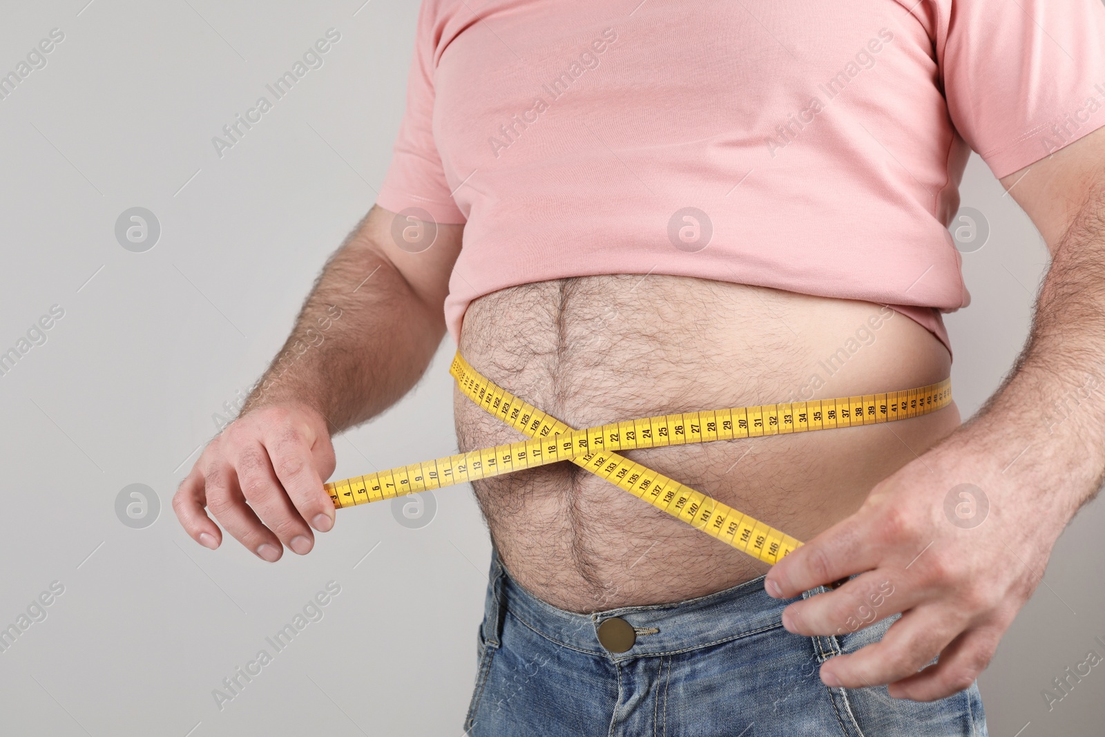 Photo of Overweight man with large belly and measuring tape on color background, closeup